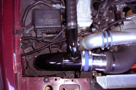 1992 Ford Crown Victoria - Engine-bay close-up of a freshly installed black cold-air intake tube and polished piping joined by blue silicone couplers, running past a…