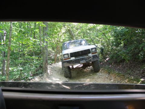 1995 Ford C-350 (Centurion Conversions) - A white pickup truck navigates a wooded trail, its front end angled towards the camera.