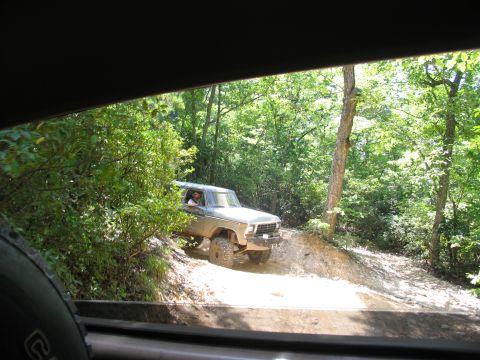 1995 Ford C-350 (Centurion Conversions) - A lifted silver truck navigates a wooded trail during an off-road excursion.