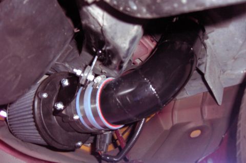 1992 Ford Crown Victoria - Under-hood close-up of a homemade cold-air intake: a black mandrel-bent tube joined by a red-striped silicone coupler and worn clamps to a…