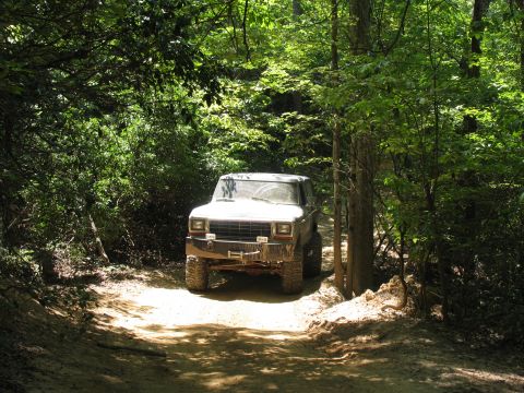 1995 Ford C-350 (Centurion Conversions) - A white Ford Bronco drives through a wooded area on a sunny day.