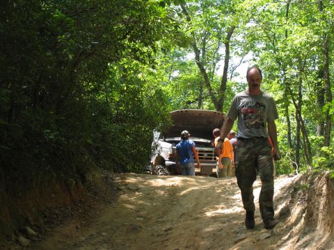 1995 Ford C-350 (Centurion Conversions) - A group of people attend to a 1995 Ford C-350 (Centurion Conversions) with its hood open on a wooded trail.