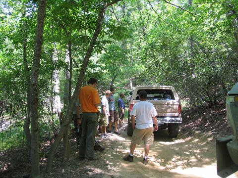 1995 Ford C-350 (Centurion Conversions) - People gather around SUVs on a dirt path surrounded by trees.