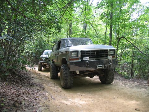 1995 Ford C-350 (Centurion Conversions) - Two off-road vehicles drive down a wooded trail in the summer.