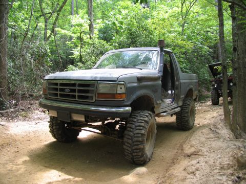 1995 Ford C-350 (Centurion Conversions) - Modified Ford Bronco on a wooded trail with another vehicle in the background.