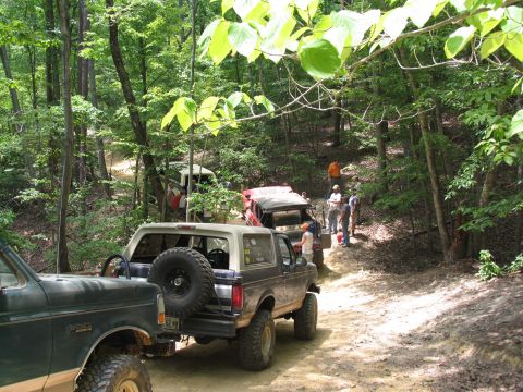 1995 Ford C-350 (Centurion Conversions) - Multiple off-road vehicles are seen on a dirt path through a forest during an event.