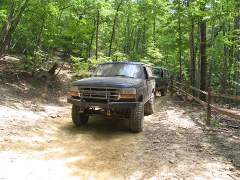 1995 Ford C-350 (Centurion Conversions) - Two off-road vehicles navigate a wooded trail in daylight.
