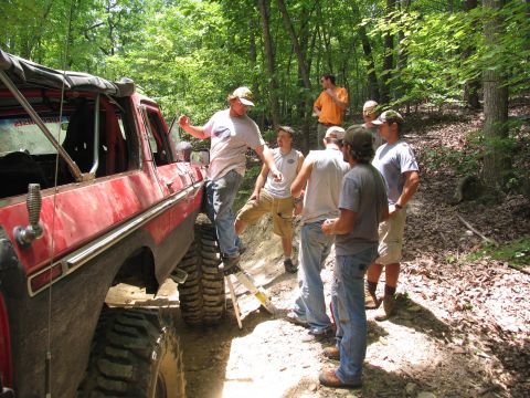 1995 Ford C-350 (Centurion Conversions) - A group of men stand around a red off-road vehicle on a wooded trail during an event in July 2006.