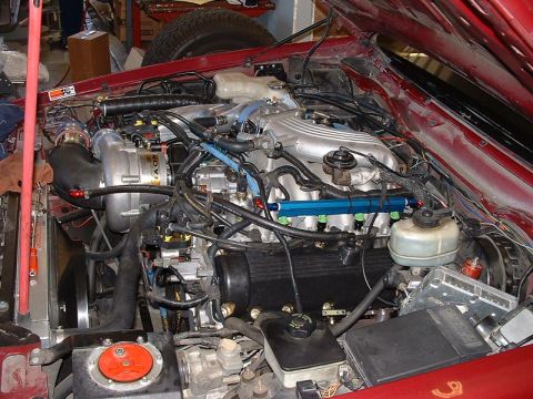 1992 Ford Crown Victoria - The engine bay of a red car showing a modified fuel-injected V-engine fitted with an aftermarket turbocharger, blue anodized fuel rails and…