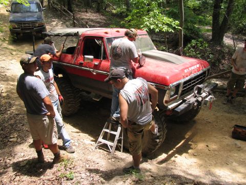 1995 Ford C-350 (Centurion Conversions) - People are working on a red pickup truck off-road, with another vehicle in the background.