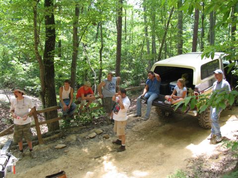 1995 Ford C-350 (Centurion Conversions) - A group of people relax near a vintage pickup truck in a wooded setting.