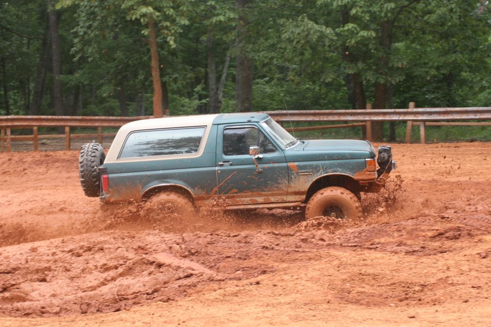 Teal Ford Bronco churning through a muddy off-road pit with spray flying