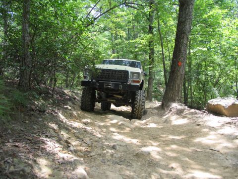 1995 Ford C-350 (Centurion Conversions) - A lifted truck navigates a challenging off-road path through a dense forest.