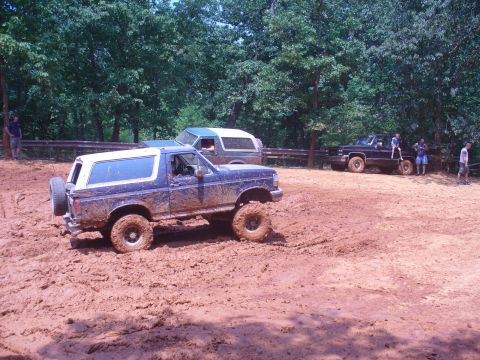 1996 Ford Bronco - Several off-road vehicles are seen navigating a muddy terrain with trees in the background.