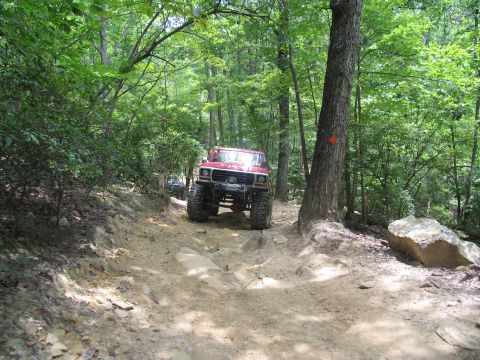 1995 Ford C-350 (Centurion Conversions) - Two off-road vehicles navigate a challenging, wooded trail with rocky terrain.