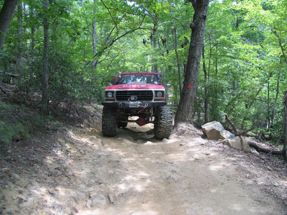 Lifted red truck with winch on a wooded dirt trail. Text on windshield reads "Uwharrie RITS July 2006"