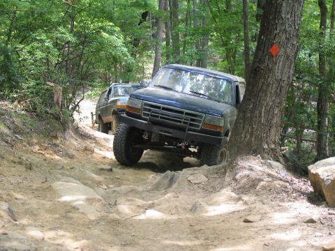 1995 Ford C-350 (Centurion Conversions) - Two trucks navigate a challenging rocky trail in a wooded area during an off-road event.