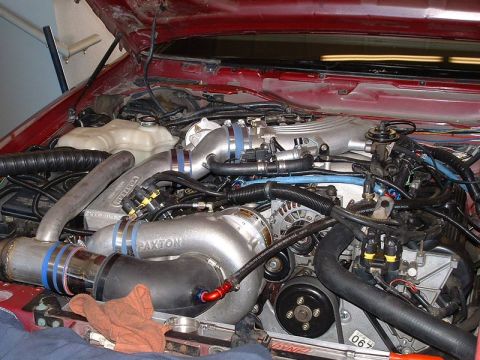 1992 Ford Crown Victoria - Engine bay of a red car with the hood up, showing a Paxton centrifugal supercharger mounted low on the passenger side and plumbed with poli…