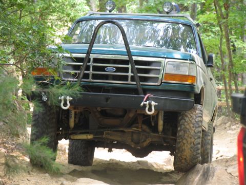 1995 Ford C-350 (Centurion Conversions) - A green Ford F-Series truck navigates a rocky trail, its front end a prominent brush guard and off-road tires.