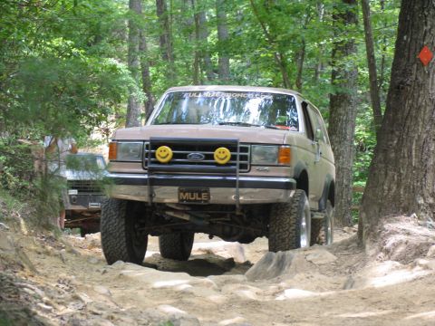 1995 Ford C-350 (Centurion Conversions) - A tan Ford Bronco navigates a challenging rocky trail, custom smiley face lights on the grille guard.