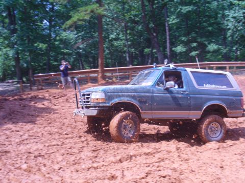 1996 Ford Bronco - A Ford Bronco navigates a muddy off-road course with a spectator capturing the action.