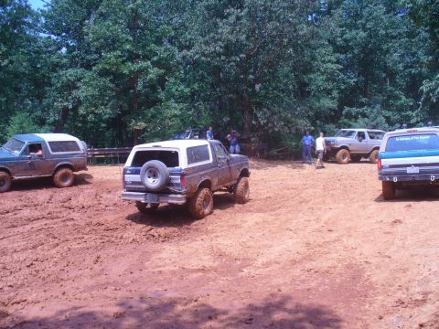 1996 Ford Bronco - Multiple Ford Broncos navigate a muddy off-road course on a sunny day.