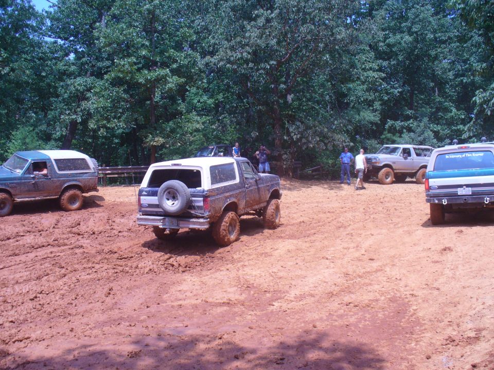 Several Ford Broncos driving in a muddy area with trees in the background
