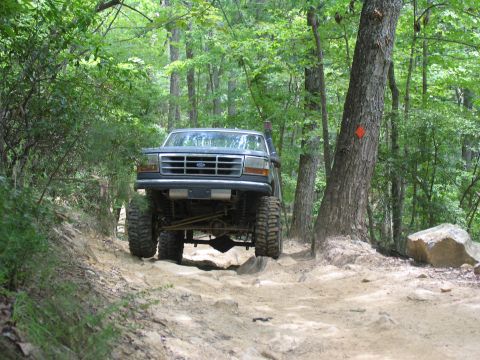1995 Ford C-350 (Centurion Conversions) - A lifted Ford truck navigates a challenging, rocky path through a wooded area.