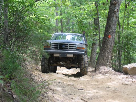 1995 Ford C-350 (Centurion Conversions) - Modified Ford F-Series truck navigates a challenging off-road path through a wooded area.