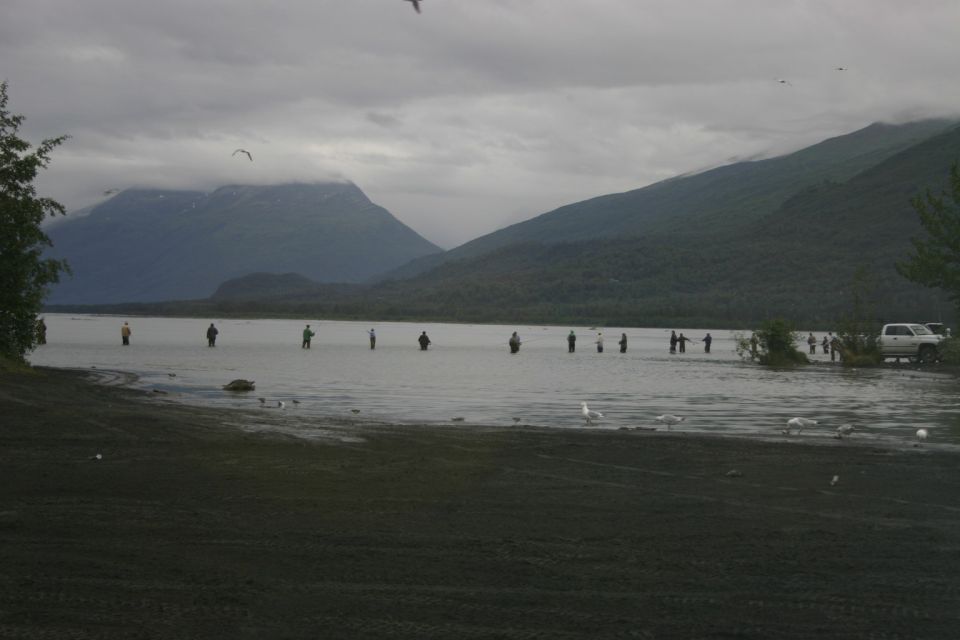 People fishing in a lake with mountains behind them. A white pickup truck is parked on the shore