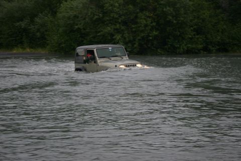 2003 Jeep TJ - A Jeep TJ navigates through a shallow river with trees in the background.