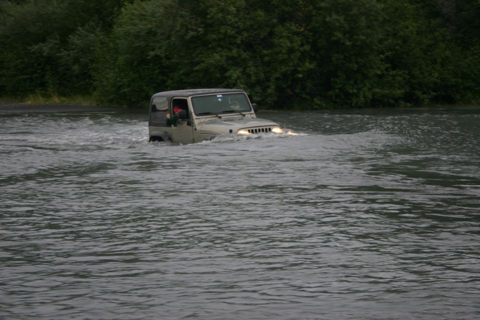 Jeep TJ driving through a river, headlights on