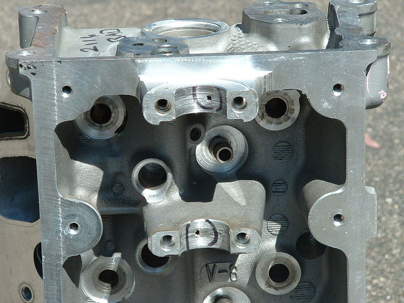 Bare aluminum OHC cylinder head showing cam caps and bolt holes, marked V-8