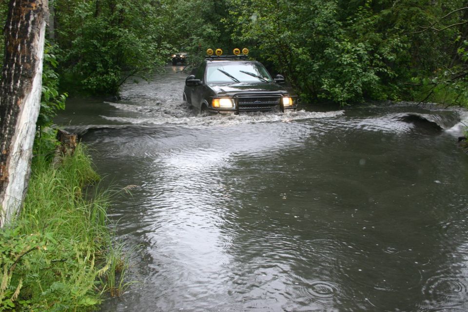 Dark SUV with roof lights driving through a shallow river, front view
