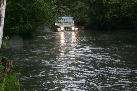 2003 Jeep TJ - A silver 2003 Jeep TJ navigates through a river, its headlights cutting through the water.