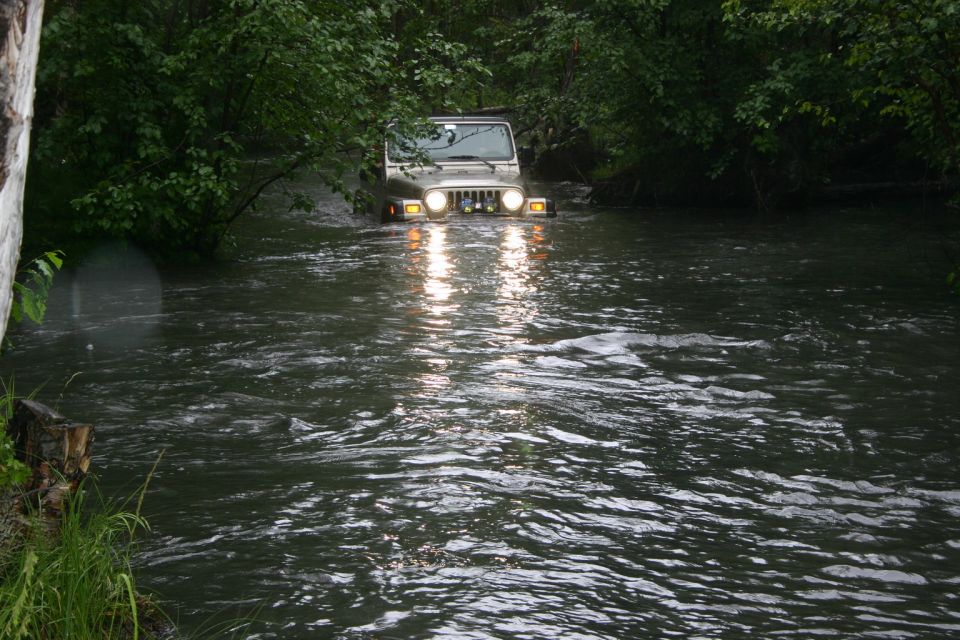 Silver 2003 Jeep TJ driving through a river with headlights on