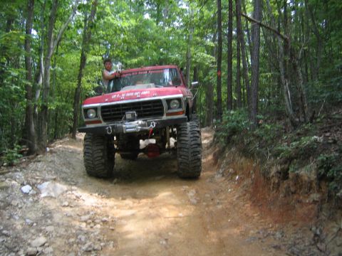 1979 Ford Bronco - This lifted truck is navigating a wooded trail with steep inclines and loose dirt.