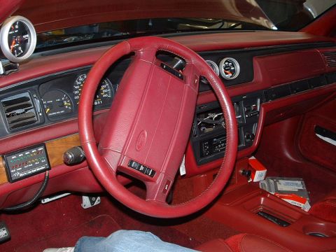 1992 Ford Crown Victoria - Interior dashboard view of a Ford sedan showing a red steering wheel with center Ford logo, matching red dash and door panels, analog gauge…