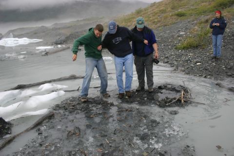 2003 Jeep TJ - People carefully cross a hazardous icy area near a glacial lake, with mountains shrouded in mist.