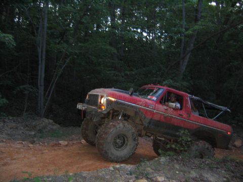 1979 Ford Bronco - A red lifted truck navigates a dirt trail through a wooded area.