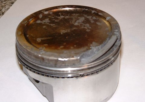 1992 Ford Crown Victoria - Close-up of a single engine piston standing on white paper on a kitchen counter, photographed from above at an angle. The dished crown is h…