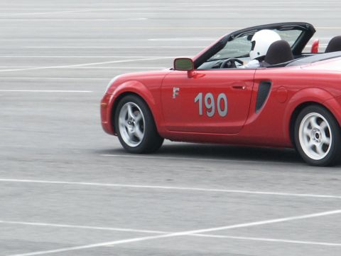 2001 Mercury Grand Marquis - A red convertible sports car with racing numbers is on a paved track, driven by someone in a helmet.