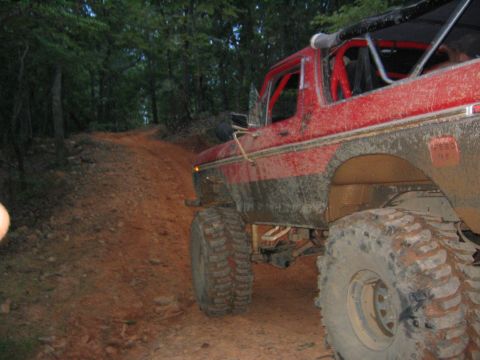 1979 Ford Bronco - A red off-road SUV navigates a muddy, uphill dirt path through a wooded area.