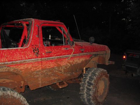 1979 Ford Bronco - A heavily muddied red SUV with a roll cage sits parked at night, with another vehicle visible in the background.