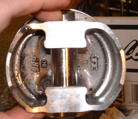 1992 Ford Crown Victoria - A forged aluminum piston held in a hand and photographed from underneath, showing the machined wrist-pin bore, ribbed skirt reliefs and cas…