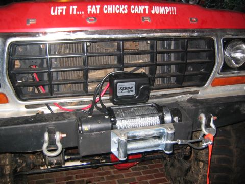 1979 Ford Bronco - The grille and bumper of a red Ford truck are visible, equipped with a winch and a humorous sticker.