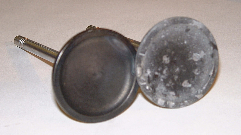 Two engine poppet valves on white background, one clean and one with gray deposits