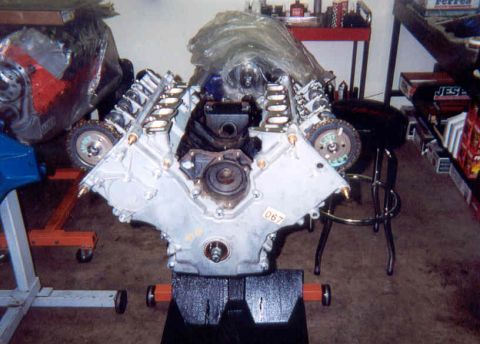 1992 Ford Crown Victoria - Front view of a partially assembled overhead-cam V8 engine on a stand in a garage, with the heads installed, valve covers off exposing the…