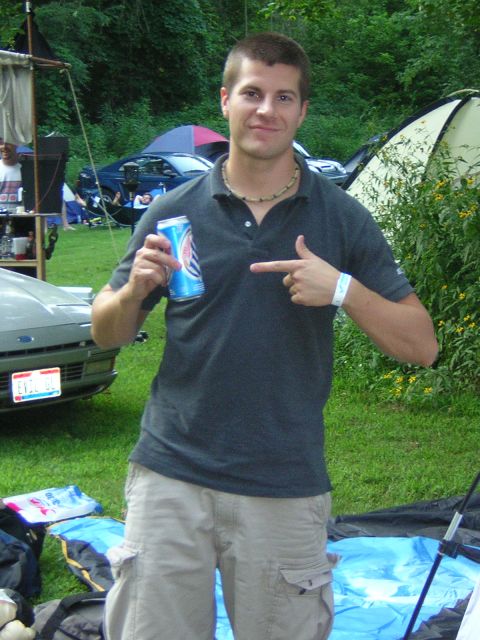 1995 Ford Probe - A man poses with a beverage at an outdoor gathering, with a car and tents visible.