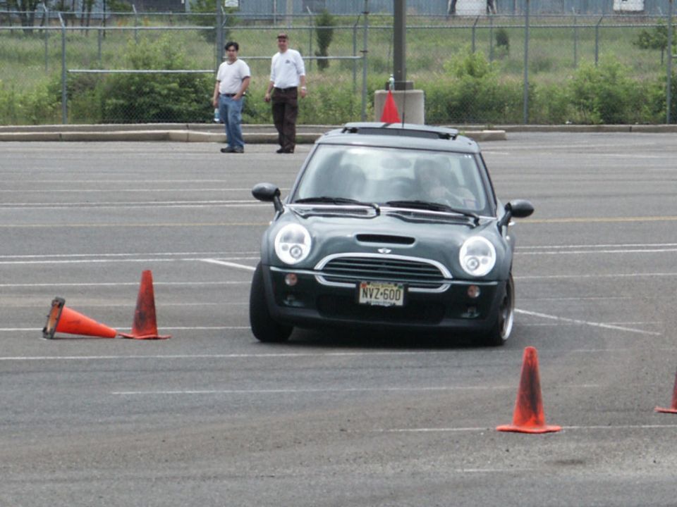 Dark green Mini Cooper S with a license plate NVZ-600 navigating an obstacle course with orange cones
